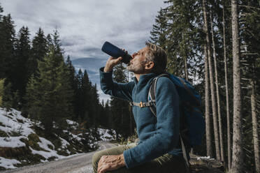 Male tourist drinking water while sitting against trees at Salzburger Land, Austria - MFF07312