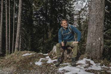 Lächelnder reifer Mann, der eine Wasserflasche hält, während er gegen Bäume im Salzburger Land, Österreich, sitzt - MFF07314