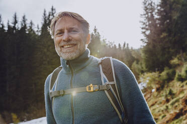 Lächelnder, gut aussehender Mann mit Rucksack im Wald gegen den Himmel im Salzburger Land, Österreich - MFF07318