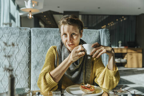 Frau mit grauen Augen trinkt Kaffee am Tisch im Hotel - MFF07326