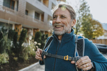 Smiling mature man standing outside hotel against sky during winter - MFF07330