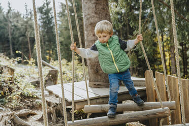 Boy balancing while doing high ropes course in forest at Salzburger Land, Austria - MFF07332