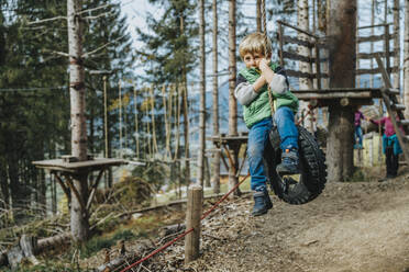 Junge schwingt mit Seil auf Reifen im Wald im Salzburger Land, Österreich - MFF07341