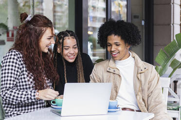 Students using laptop while sitting together at sidewalk cafe - PNAF00710