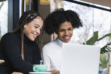 Lächelnde Studenten, die einen Laptop in einem Straßencafé benutzen - PNAF00733