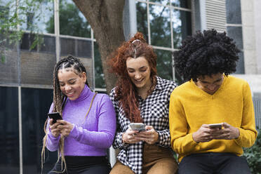 Lächelnde Freunde, die ihr Handy benutzen, während sie in der Universität sitzen - PNAF00734