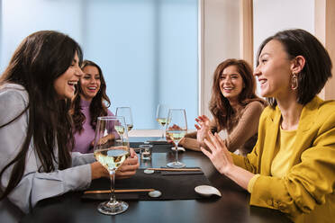 Female friends with wine glasses laughing while sitting at table in restaurant - AODF00280