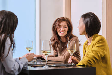 Young female friends with wine glasses while sitting at table in restaurant - AODF00281