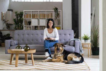 Lächelnde junge Frau mit Haushund im Wohnzimmer - GIOF11302