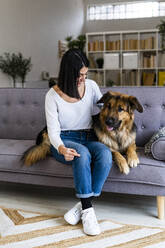 Woman with German shepherd sitting on sofa at home - GIOF11304