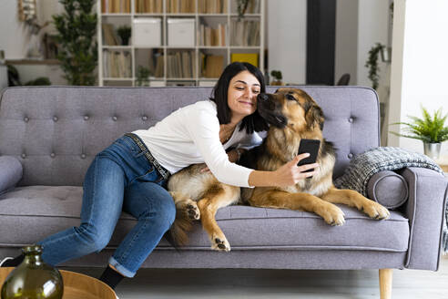 Lächelnde junge Frau macht Selfie mit Hund im Wohnzimmer - GIOF11307