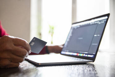 Älterer Mann kauft zu Hause mit Laptop und Kreditkarte online ein - MAMF01628