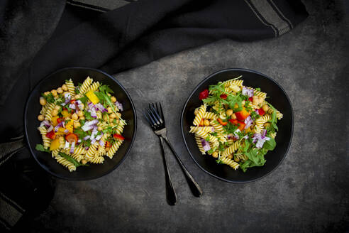 Studioaufnahme von zwei Schüsseln Fusilli-Nudelsalat mit Kichererbsen, Paprika, Rucola, spanischen Zwiebeln, Basilikum und Petersilie - LVF09083