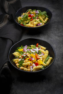 Studioaufnahme von zwei Schüsseln Fusilli-Nudelsalat mit Kichererbsen, Paprika, Rucola, spanischen Zwiebeln, Basilikum und Petersilie - LVF09084