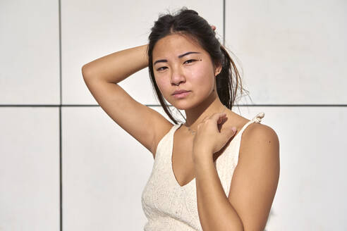 Beautiful woman with hand behind head against wall on sunny day - VEGF03939