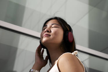 Asiatische Frau hört Musik über Kopfhörer im Freien - VEGF03944