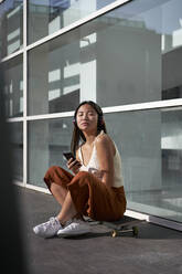 Junge Frau mit Smartphone hört Musik über Kopfhörer an einem sonnigen Tag - VEGF03949