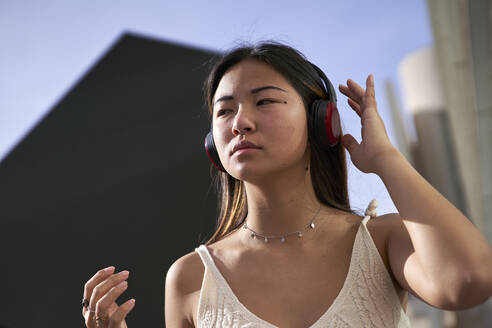 Asiatische Frau schaut weg, während sie an einem sonnigen Tag über Kopfhörer Musik hört - VEGF03956