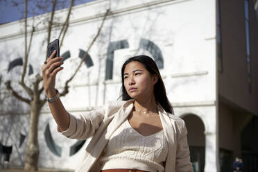 Stylish woman taking selfie through mobile phone on sunny day - VEGF03958