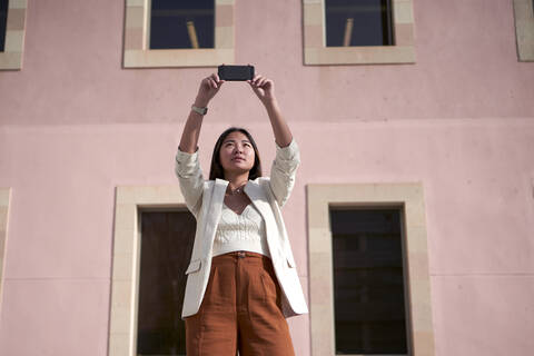 Stylish woman taking selfie on smart phone against building stock photo