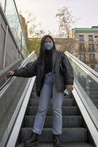 Junge Frau, die während der COVID-19 auf einer Rolltreppe steht, lizenzfreies Stockfoto