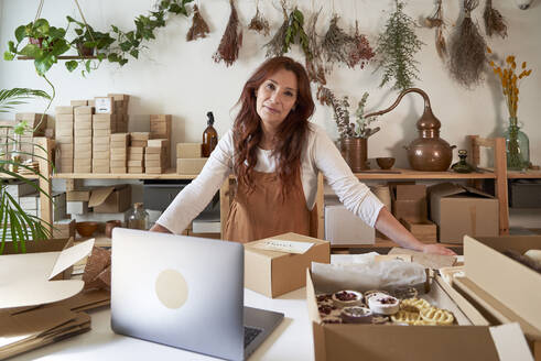 Lächelnde Unternehmerin, die sich in einer Werkstatt auf einen Tisch stützt - VEGF03999