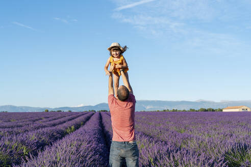 Father holding aloft baby daughter in vast lavender field during summer - GEMF04700