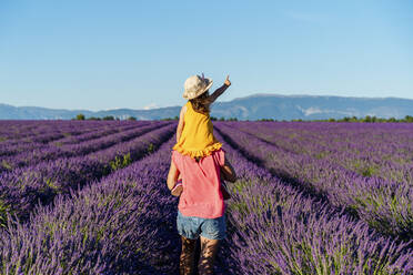 Mother piggybacking little daughter in vast summer lavender field - GEMF04708