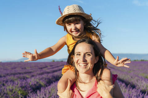 Portrait of mother piggybacking little daughter in vast summer lavender field stock photo