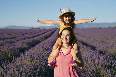 Portrait of mother piggybacking little daughter in vast summer lavender field - GEMF04711