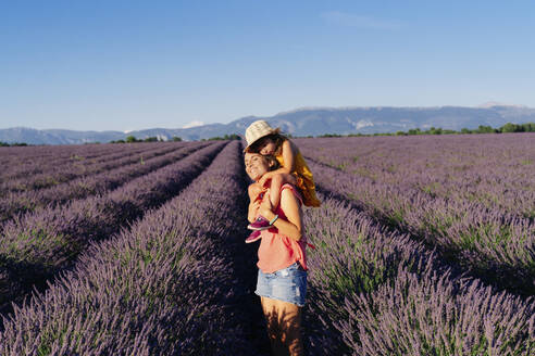 Mother piggybacking little daughter in vast summer lavender field - GEMF04712