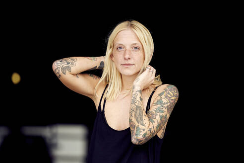 Tattooed woman with hand in hair standing at parking garage - UKOF00125