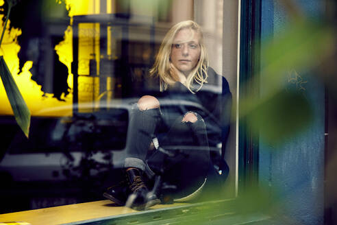 Thoughtful woman sitting on window sill while looking away - UKOF00131