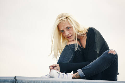 Blond woman sitting at rooftop with head on hand stock photo