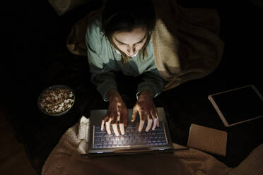 Woman using laptop while lying by popcorn and digital tablet at home - AFVF08209