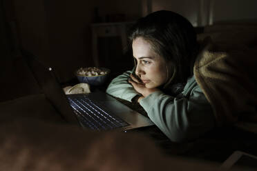 Woman with popcorn watching movie on laptop in dark while relaxing at home - AFVF08210