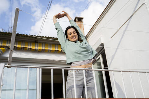 Lächelnde Frau, die ihre Hand ausstreckt, während sie auf einem Balkon steht, lizenzfreies Stockfoto