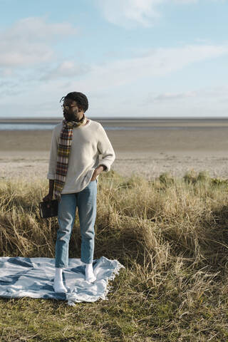 Man with hand in pocket standing on blanket while looking away against cloudy sky stock photo