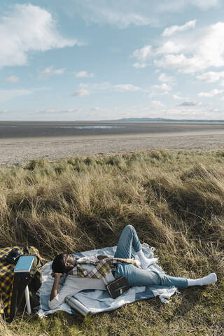 Junger Mann liegt auf einer Decke und schaut auf den Strand, lizenzfreies Stockfoto