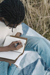 Young man writing on his diary while sitting at beach - BOYF01845