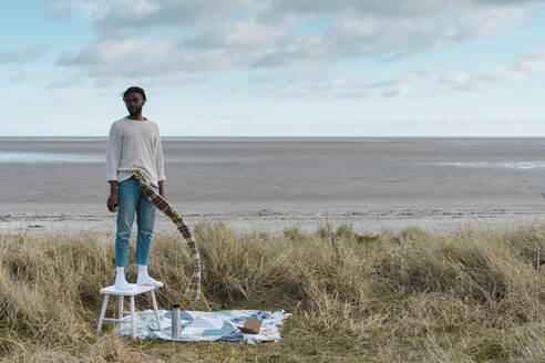 Young man looking away while standing on stool at beach - BOYF01864