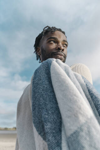 Man with blanket looking away against cloudy sky stock photo