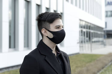 Young male entrepreneur in protective face mask against office building - FLLF00585