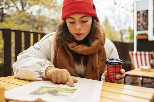 Frau mit Kaffeetasse, die in einem Straßencafé sitzt und Zeitung liest - OYF00317