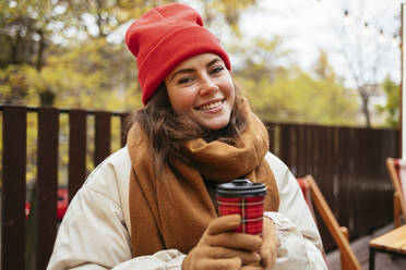 Woman with disposable coffee cup smiling while sitting at sidewalk cafe - OYF00328