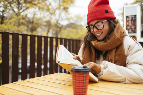 Frau lächelt beim Lesen eines Buches in einem Straßencafé, lizenzfreies Stockfoto