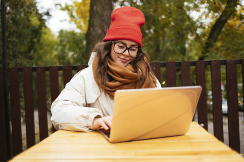 Lächelnde Frau, die einen Laptop benutzt, während sie in einem Straßencafé sitzt, lizenzfreies Stockfoto