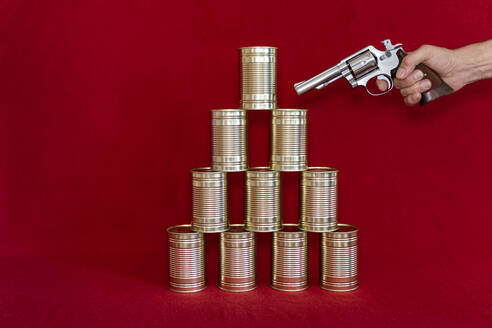 Human hand holding gun against stack of tin cans - DRF01760