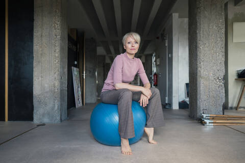 Blonde Frau sitzt auf einem Fitnessball in einer Loftwohnung, lizenzfreies Stockfoto