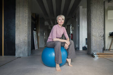 Blonde Frau sitzt auf einem Fitnessball in einer Loftwohnung - MOEF03572